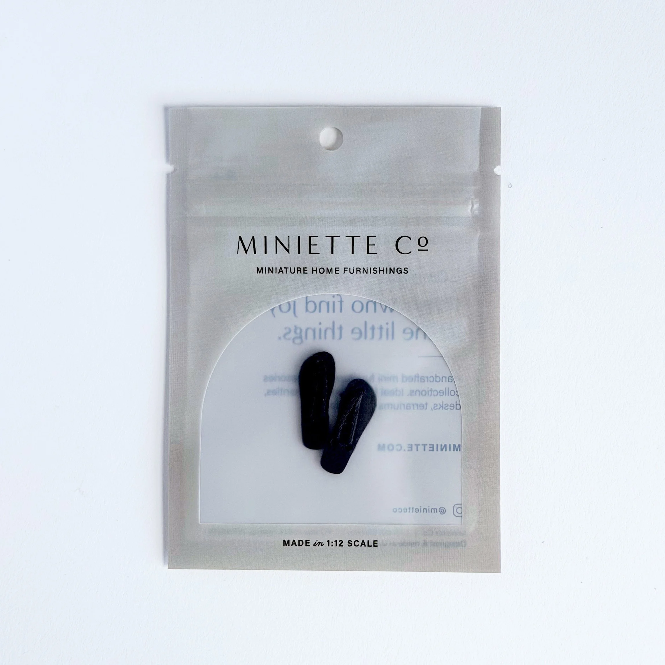 Close-up of miniature black flip flops showing scale and detail
