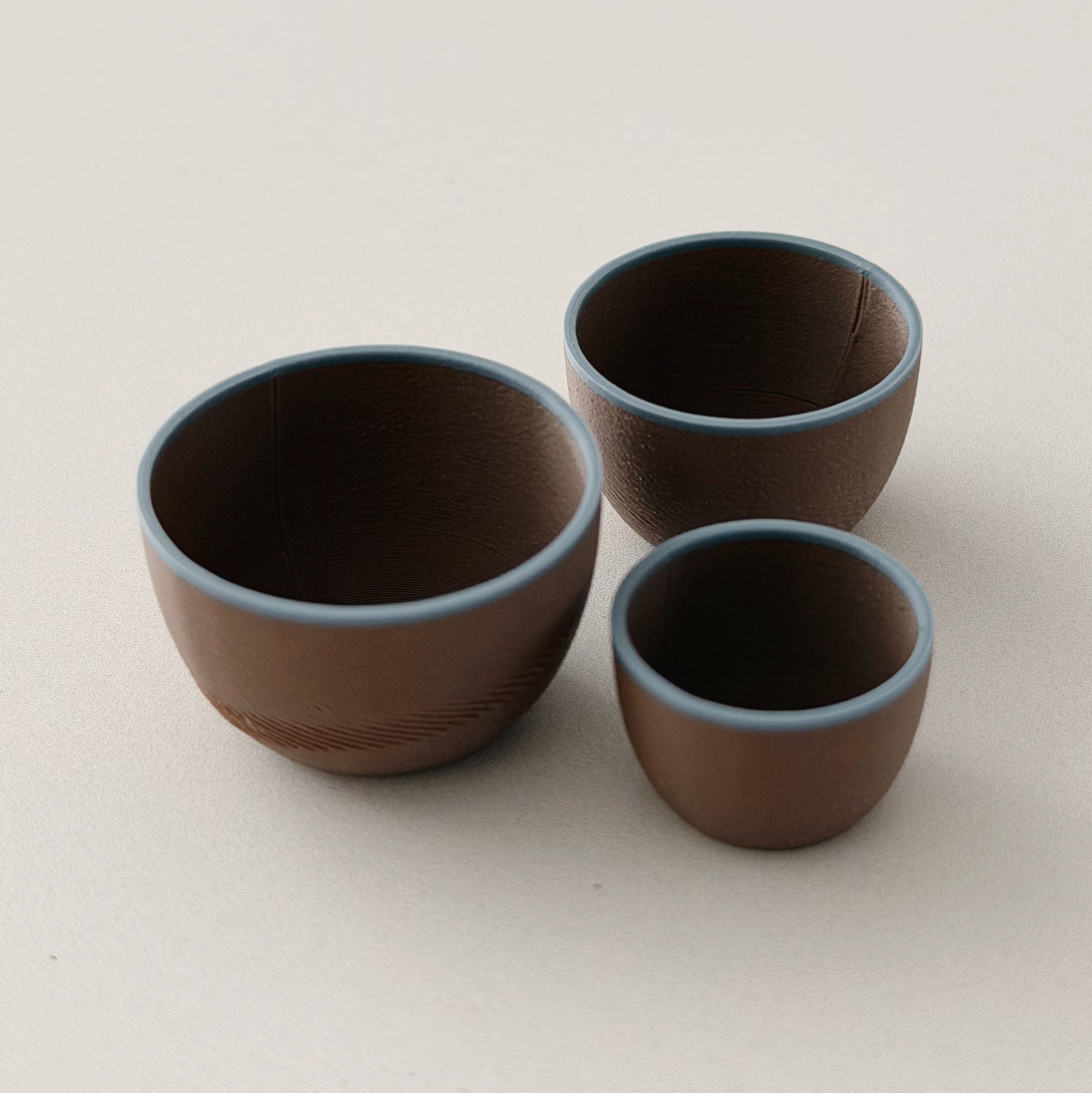 Three brown 1:12 scale miniature nesting bowls with soft blue rims