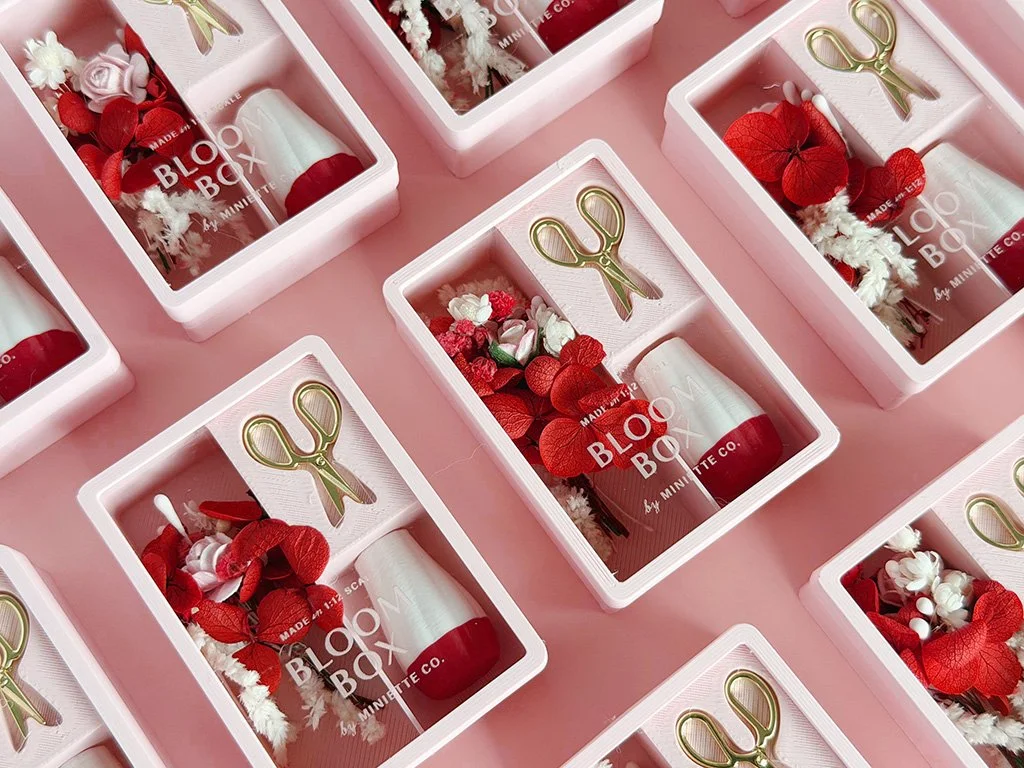 Valentine Bloom Box miniature floral arrangement with blush and red flowers, white vase, and gold scissors