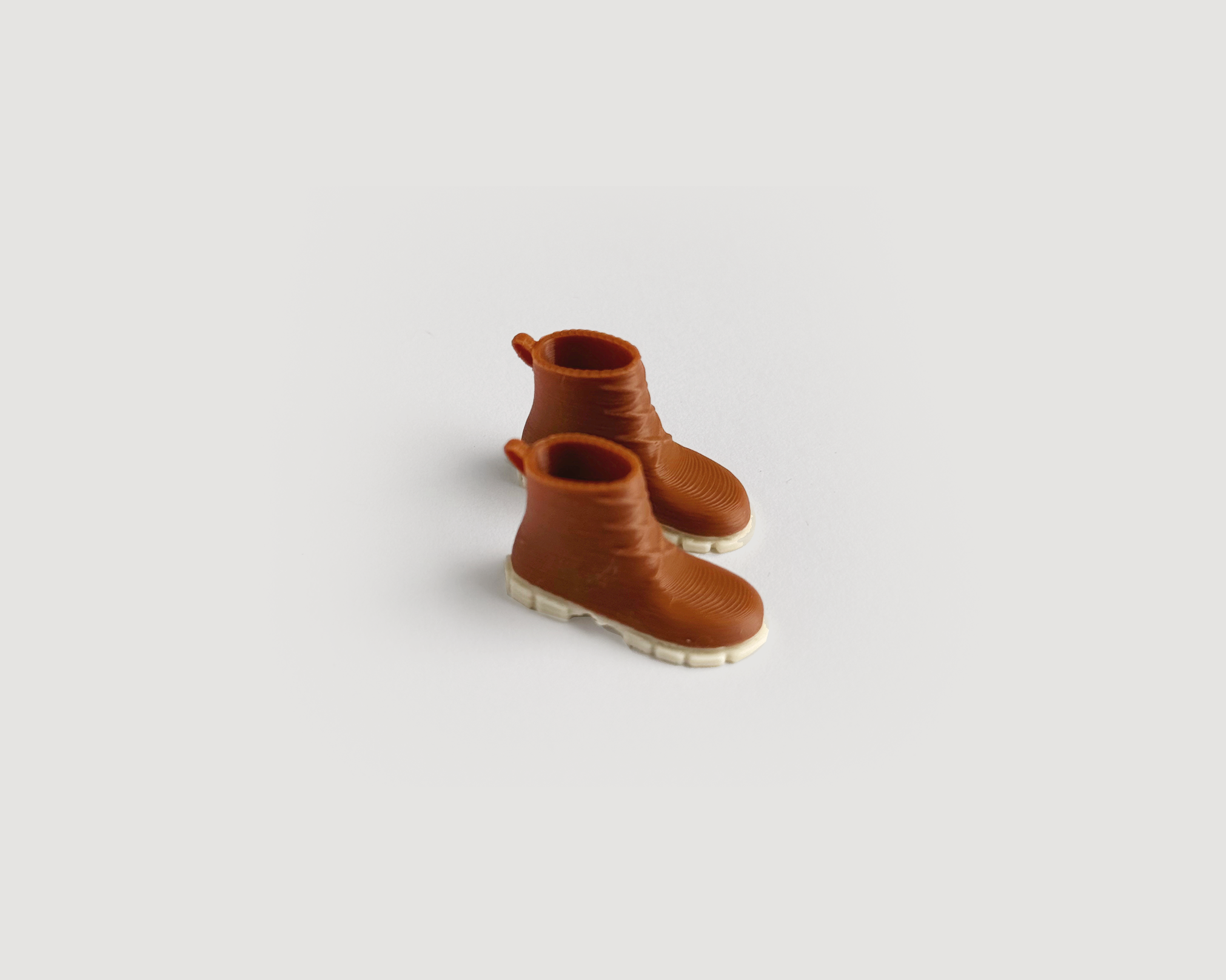 Pair of miniature brown dollhouse boots in 1:12 scale. Plastic footwear accessory for fall and winter dollhouse décor.