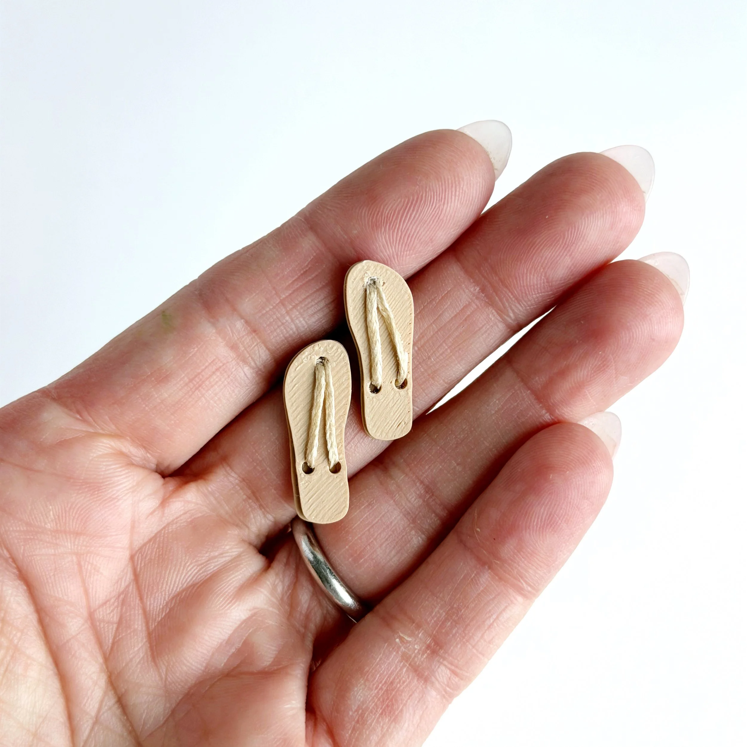 Hand holding tan miniature flip flops to show 1:12 scale size
