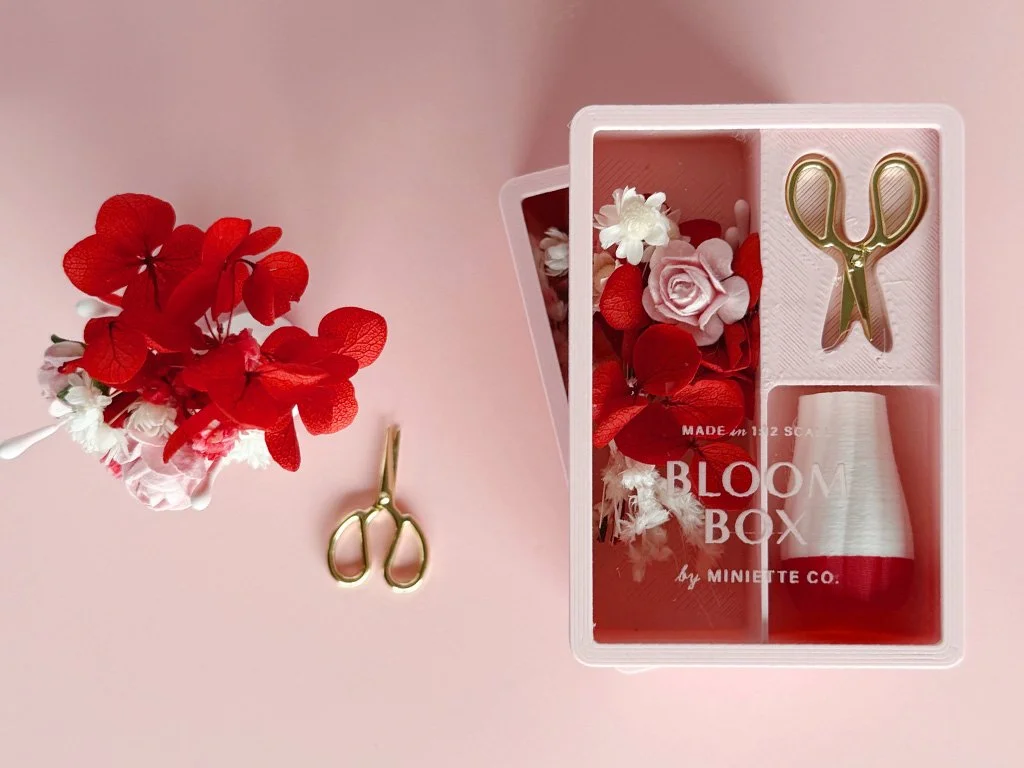 Close-up of miniature Valentine flowers with blush roses, red accents, and gold scissors