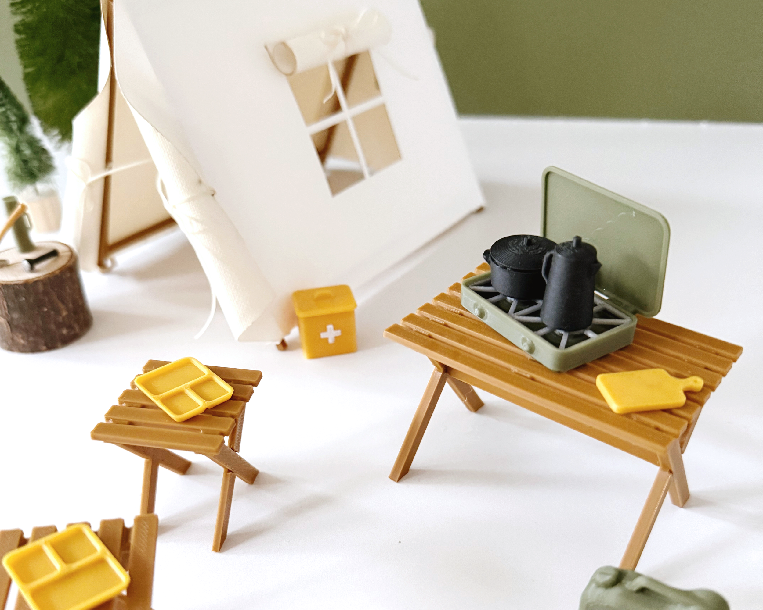 Miniature camping scene with 1:12 scale dollhouse accessories including log, axe, and table next to a tent