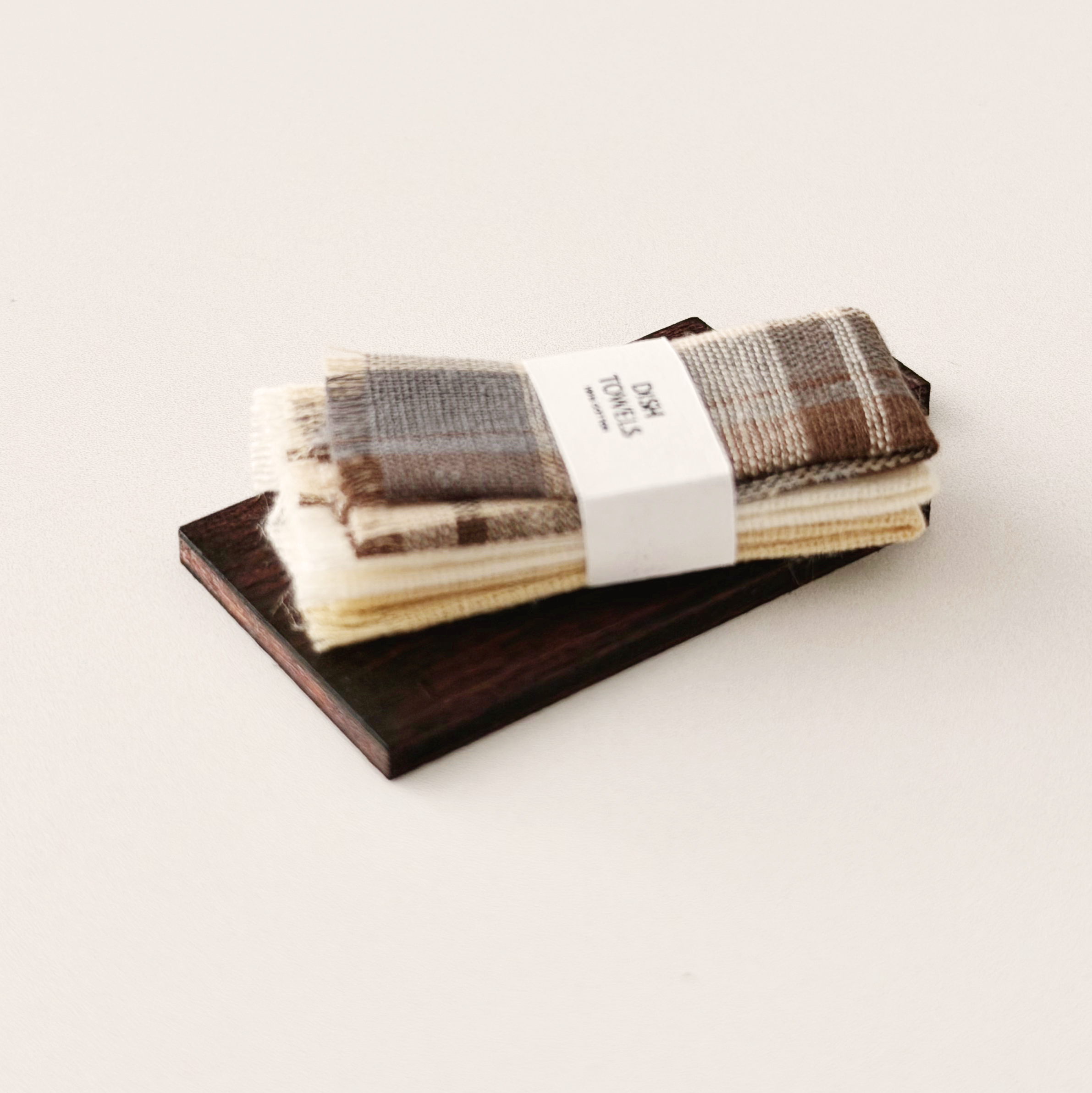 Dark wood miniature cutting board with three warm neutral dollhouse dish towels