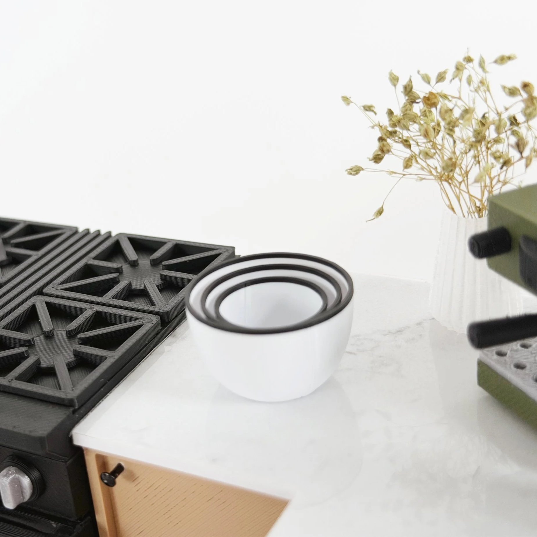 Miniature white nesting bowls with black trim styled on a dollhouse kitchen countertop.