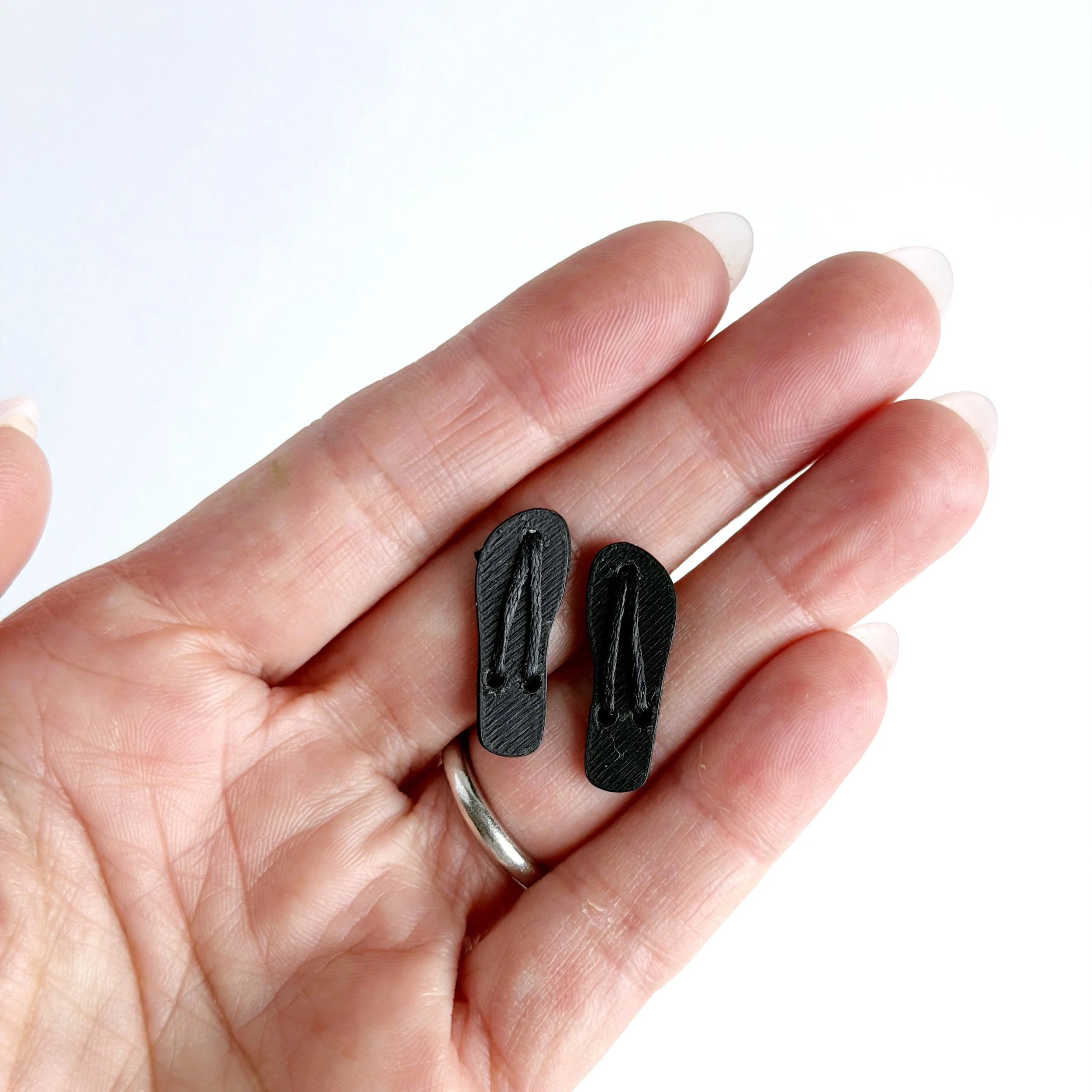 Hand holding black miniature flip flops to show 1:12 scale size