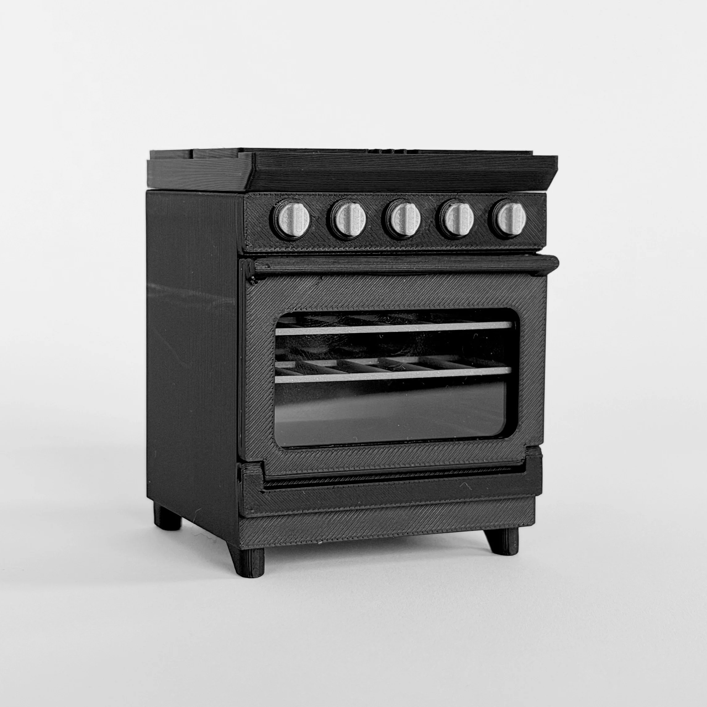 Black 1:12 scale miniature stove and oven with 4-burner stovetop, shown with oven door open and interior racks visible.