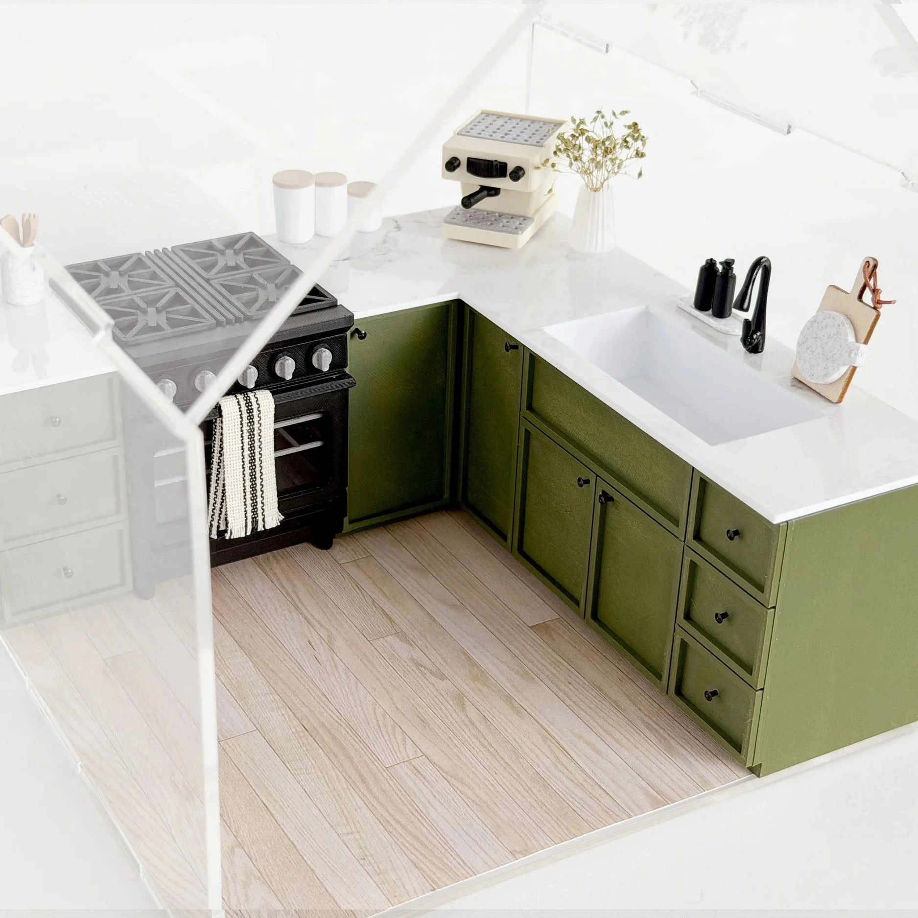 Modern miniature kitchen setup featuring olive green cabinets and oven, styled inside a clear acrylic dollhouse display. (Copy)