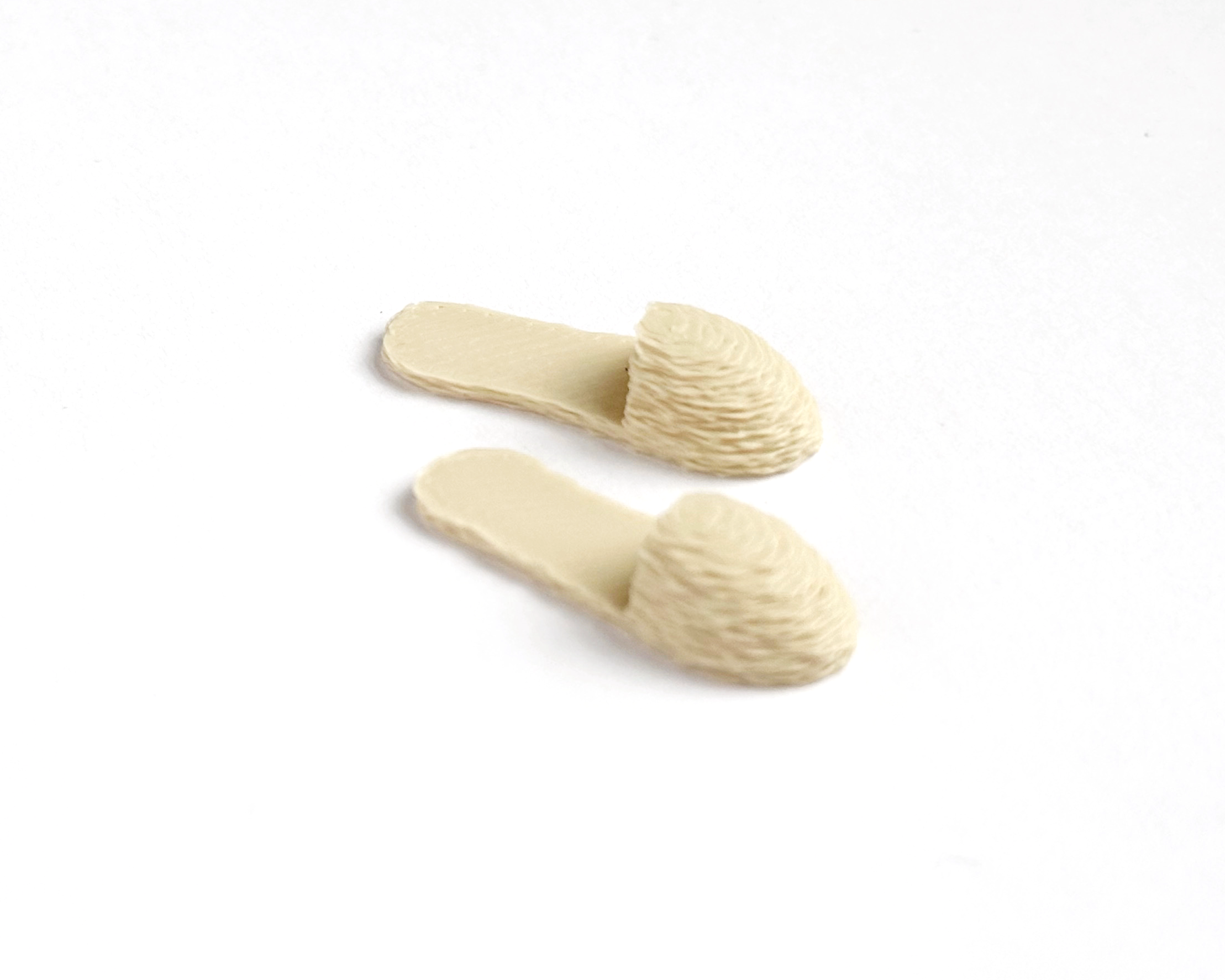 Tiny dollhouse slippers in neutral ivory, perfect for adding warmth and comfort to miniature bedroom or living room displays.