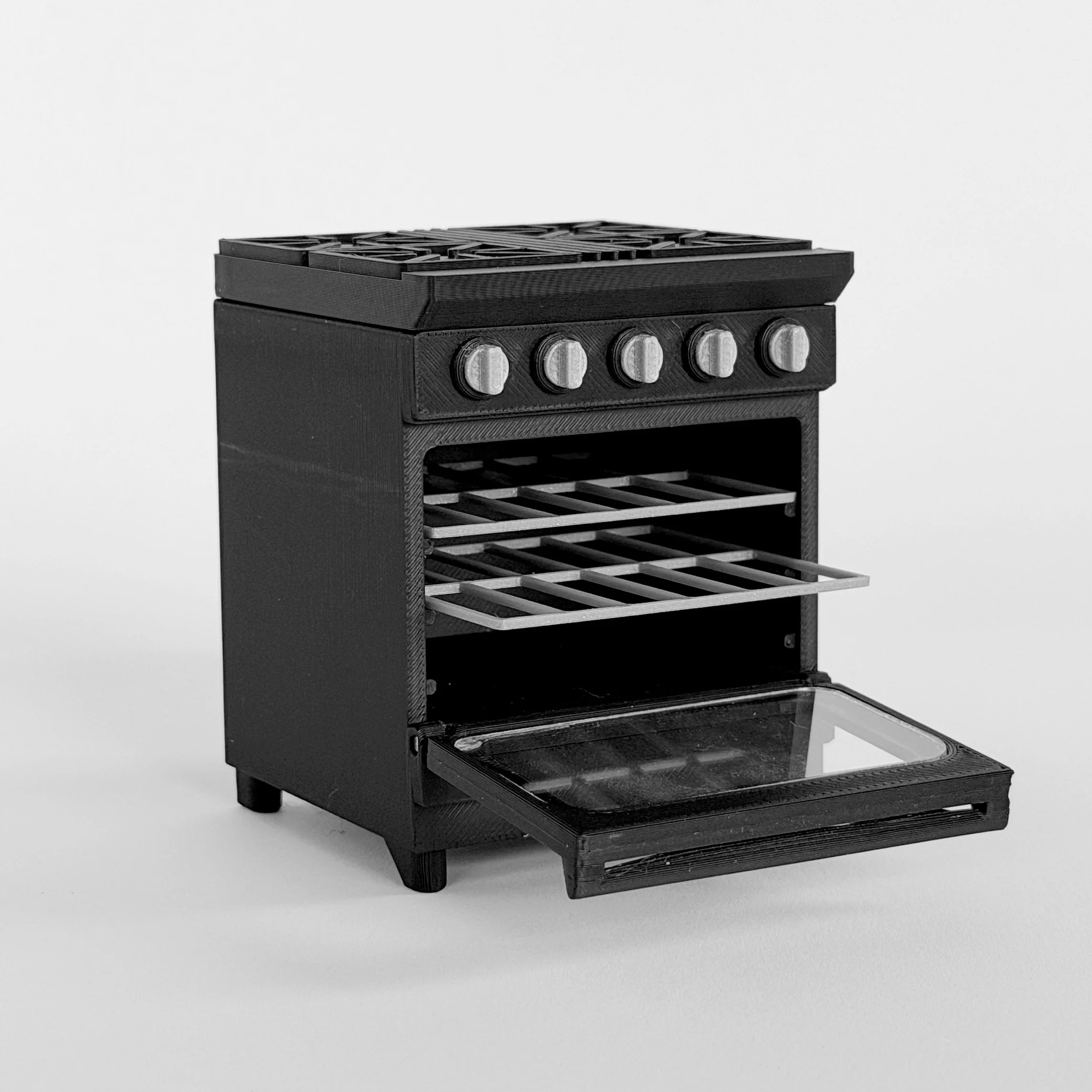 Close-up of miniature black dollhouse oven with opening door and removable metal-style racks.