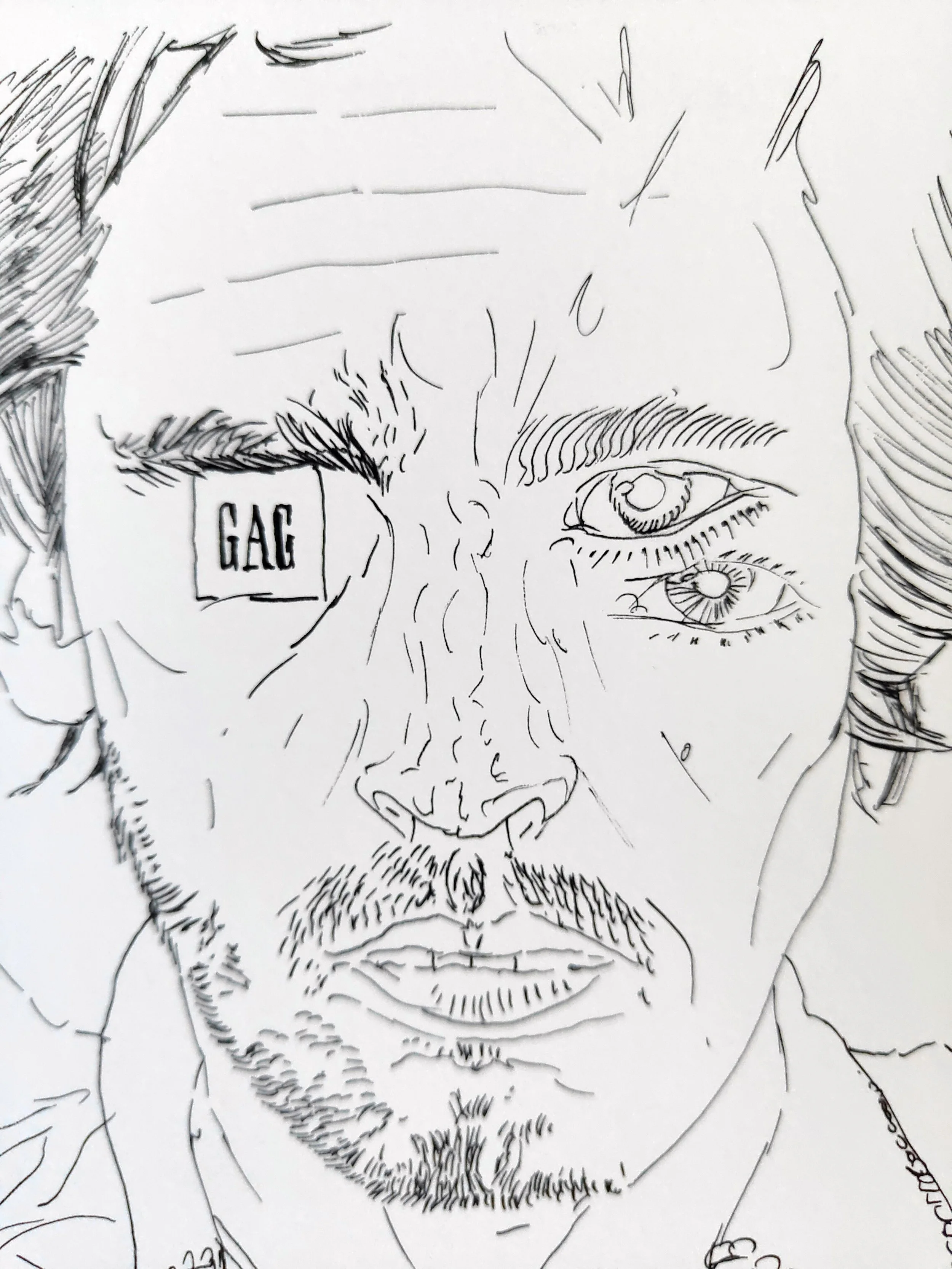 Willcott artwork, black and white line drawing of a man's face showing one eye, part of his nose, beard, and mustache, with side hair and a hand holding a small rectangular object with the word "GAG" on it.