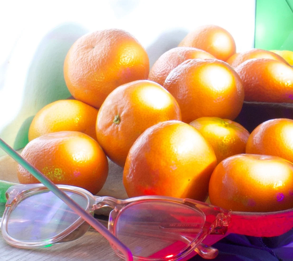 A bowl of fresh oranges with a pair of pink sunglasses resting in front of it.