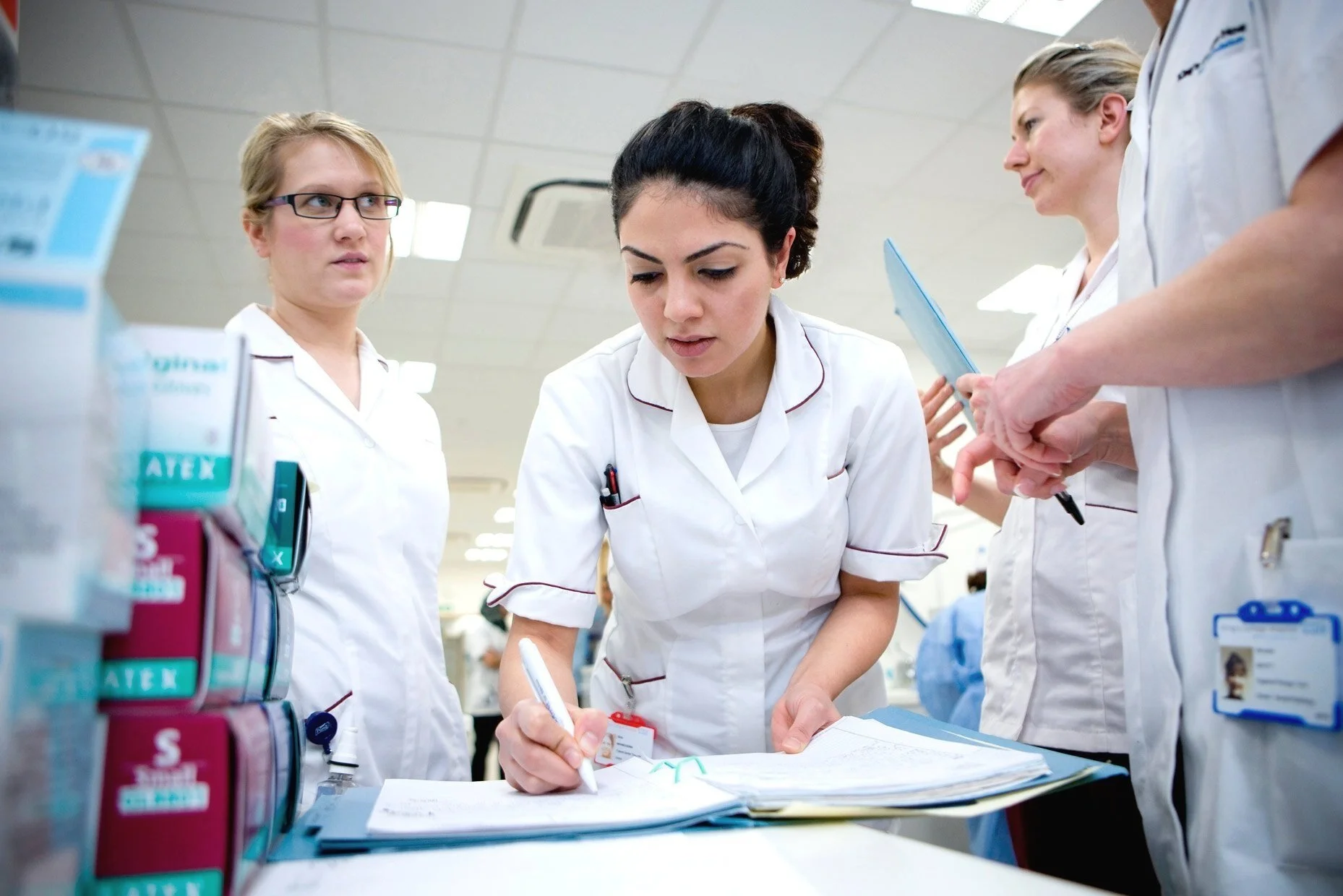 Group of female healthcare professionals in white uniforms working together in a medical setting, reviewing documents.