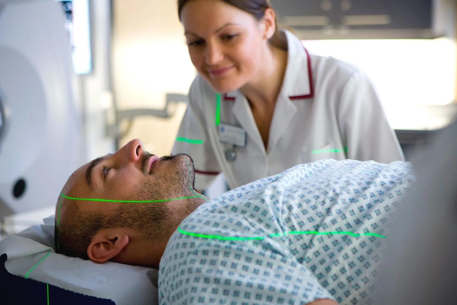 A man lying in a scanner with green laser lights tracking his body, depicting advanced imaging technology in a clinical or research setting.