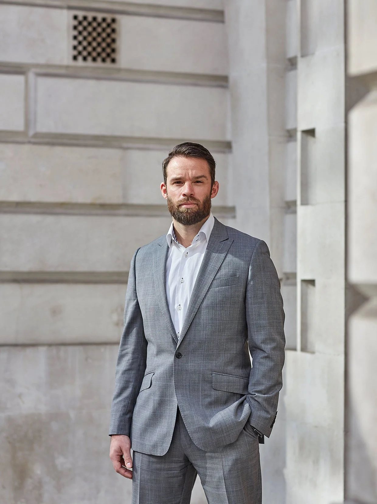 A suited businessman standing confidently against a grey urban building, representing modern corporate style and professionalism.