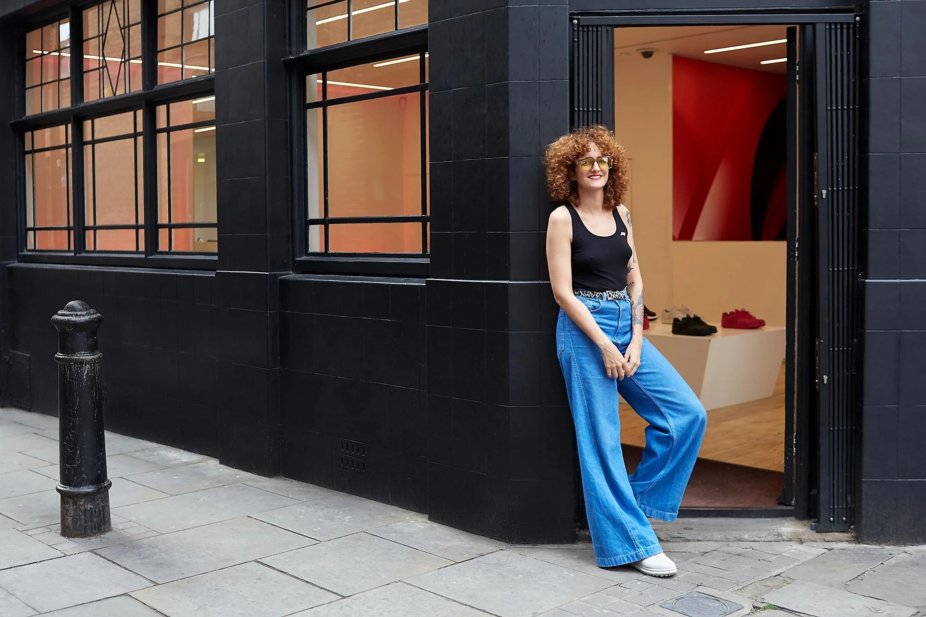 A stylish shop worker standing outside her minimalist shoe store in an urban setting, reflecting modern retail and independent fashion.