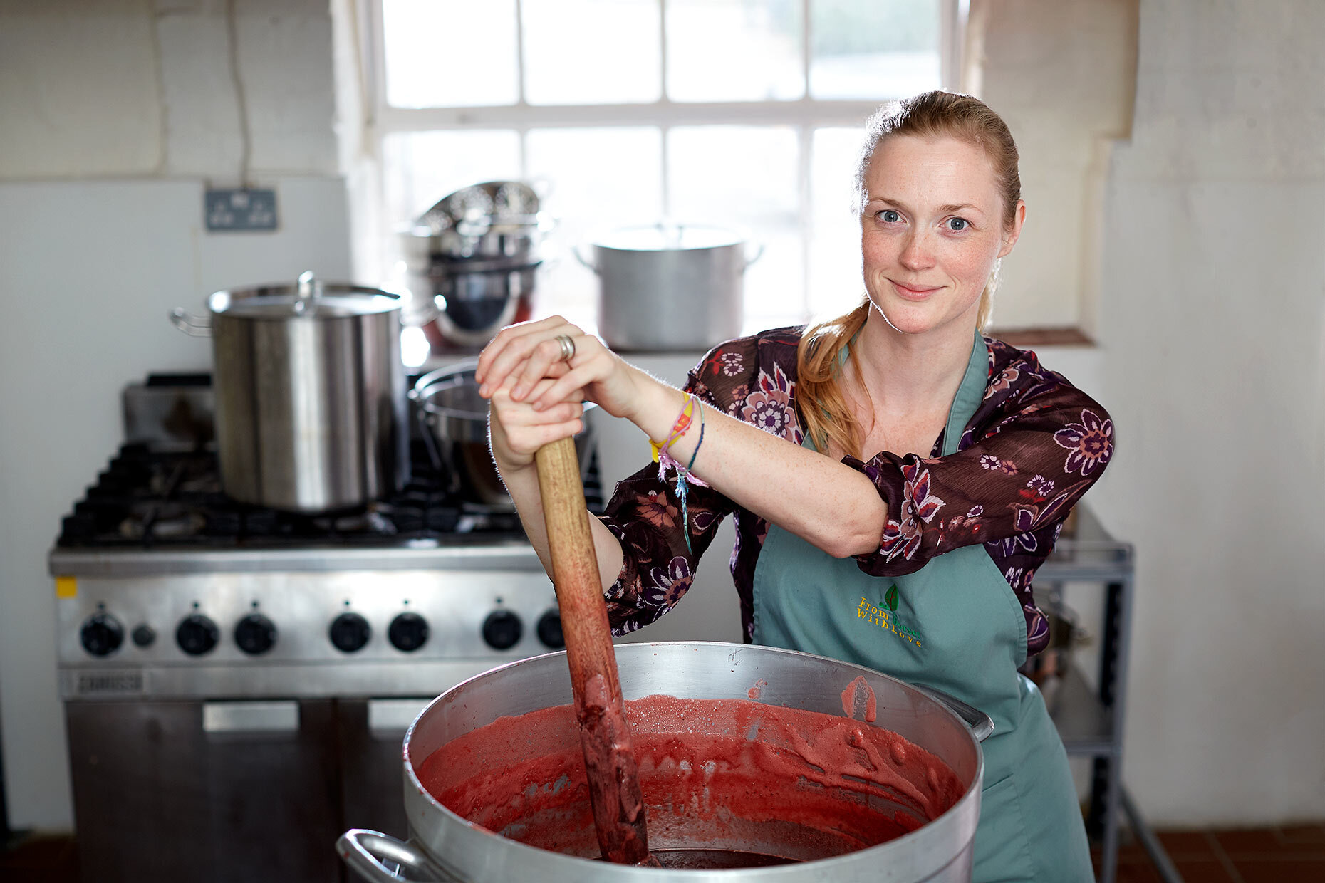 Woman stirring a large pot of red liquid in a kitchen setting.