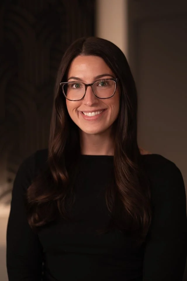 Taylor Scotti wearing glasses, and a black top, smiling at the camera indoors.