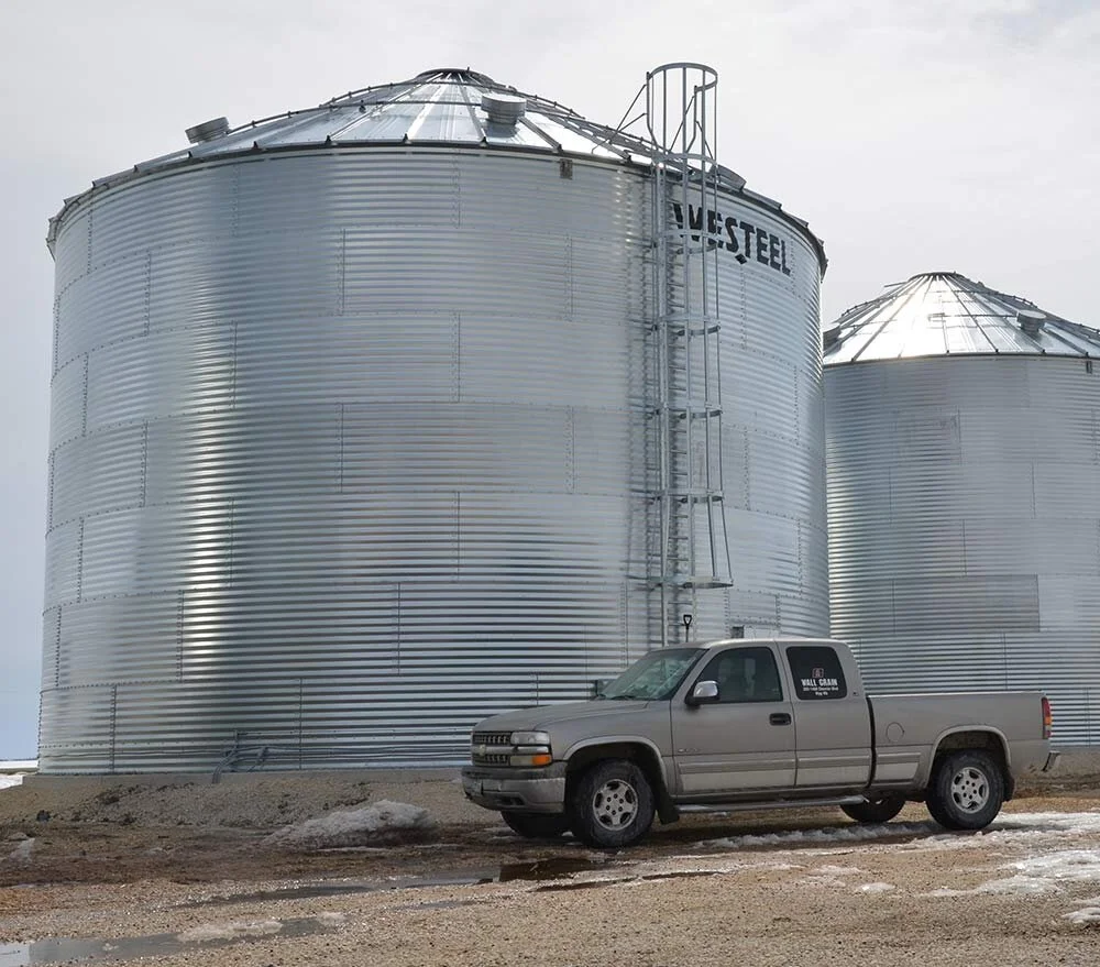 Large Westeel grain storage bins beside a Wall Grain Handling Systems service truck.