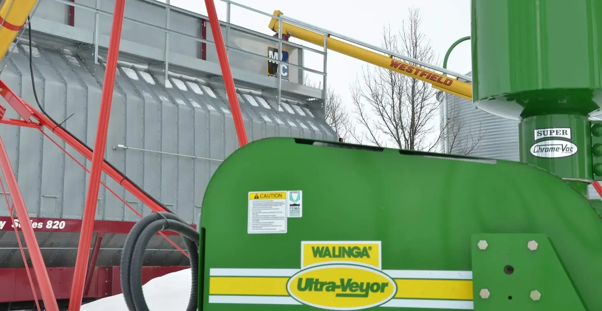 Walinga Ultra-Veyor grain conveying system positioned beside a grain dryer and storage bins, supporting efficient grain transfer and handling operations on a farm.