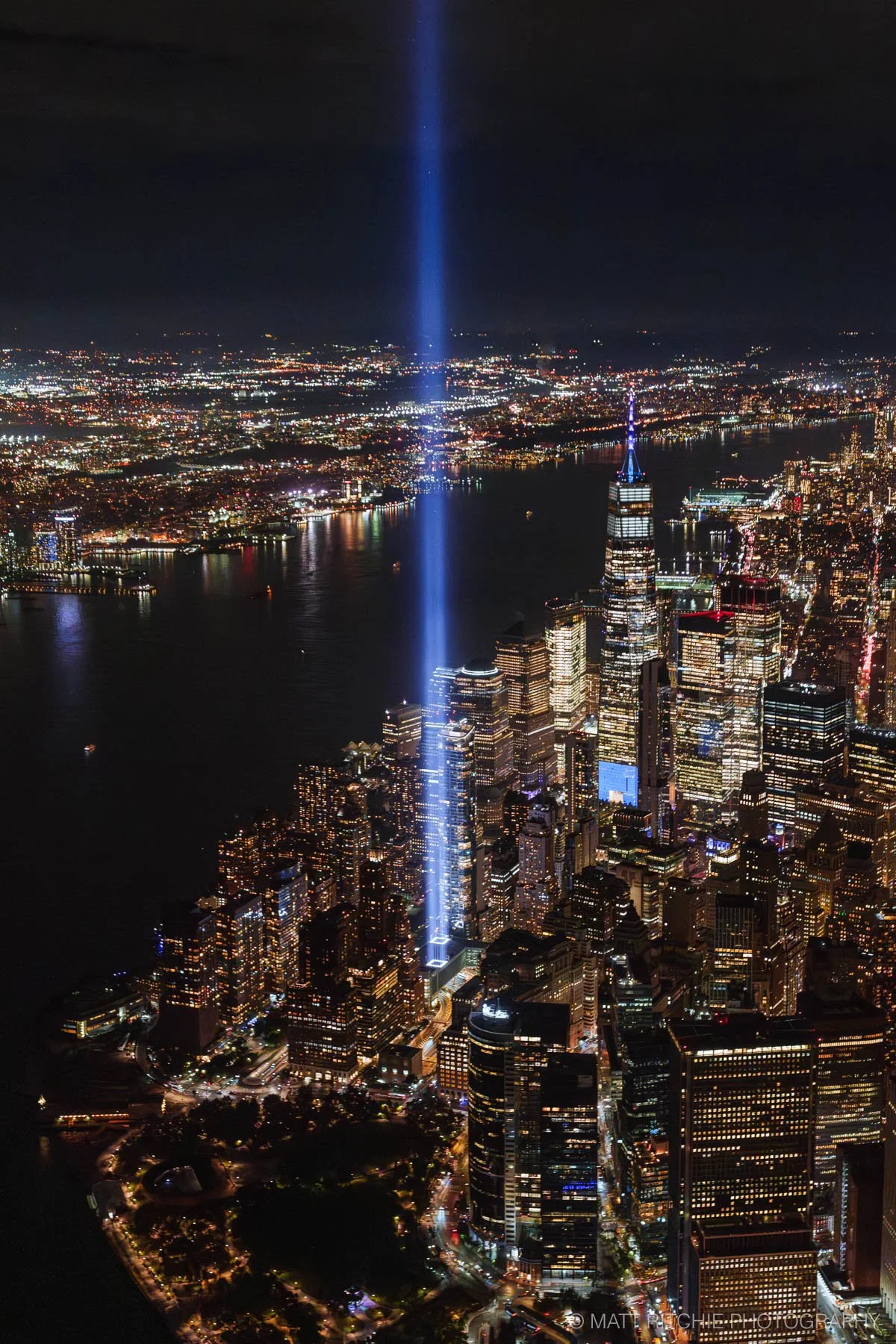 Aerial view of the Tribute in Light memorial illuminating the New York City skyline at night, captured from a FlyNYON helicopter.