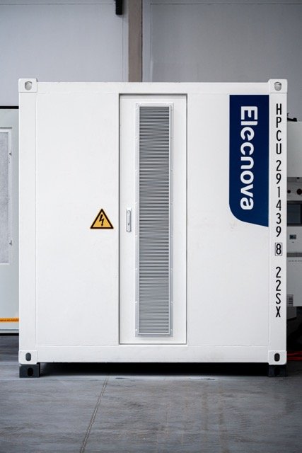 En hvit maskin med logo og tekst, inkludert en gul advarselskilt, plassert på en industriell gulvflate.