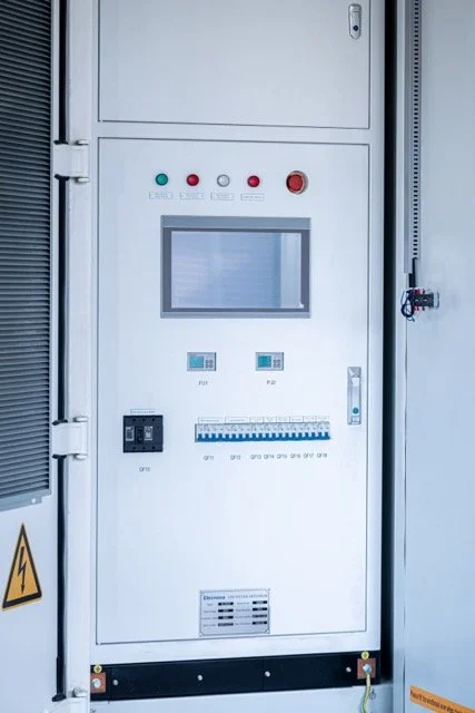 Elektrisk kontrollskap med display, indikatorlamper, brytere og sikringsskap i et industrilokale.