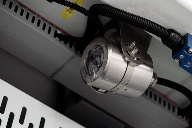 Nærbilde av en industriell kamerakobling montert på en metallramme, med ledninger og kabler for tilkobling.