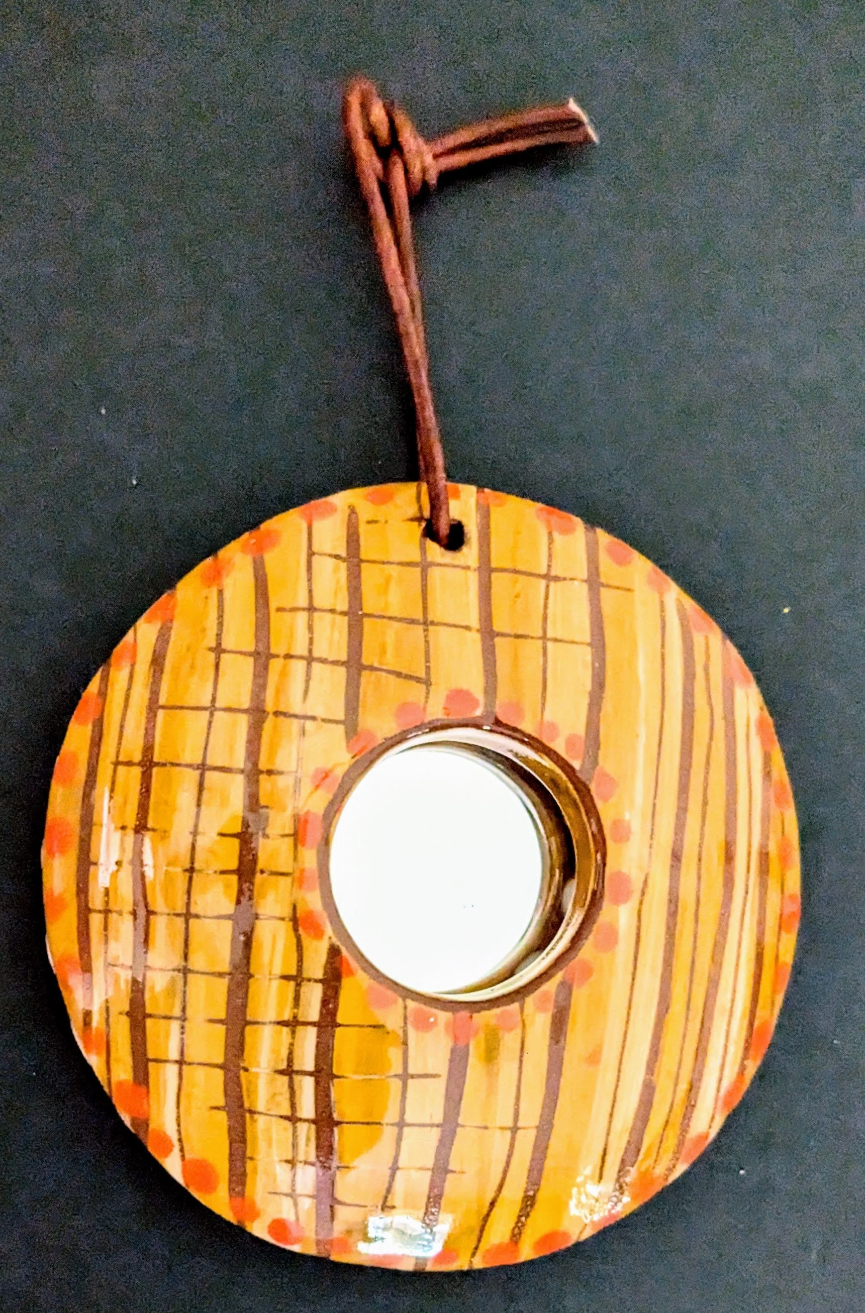 A small circular ceramic framed mirror hand painted with yellow and orange glaze with a sgraffito design over top.