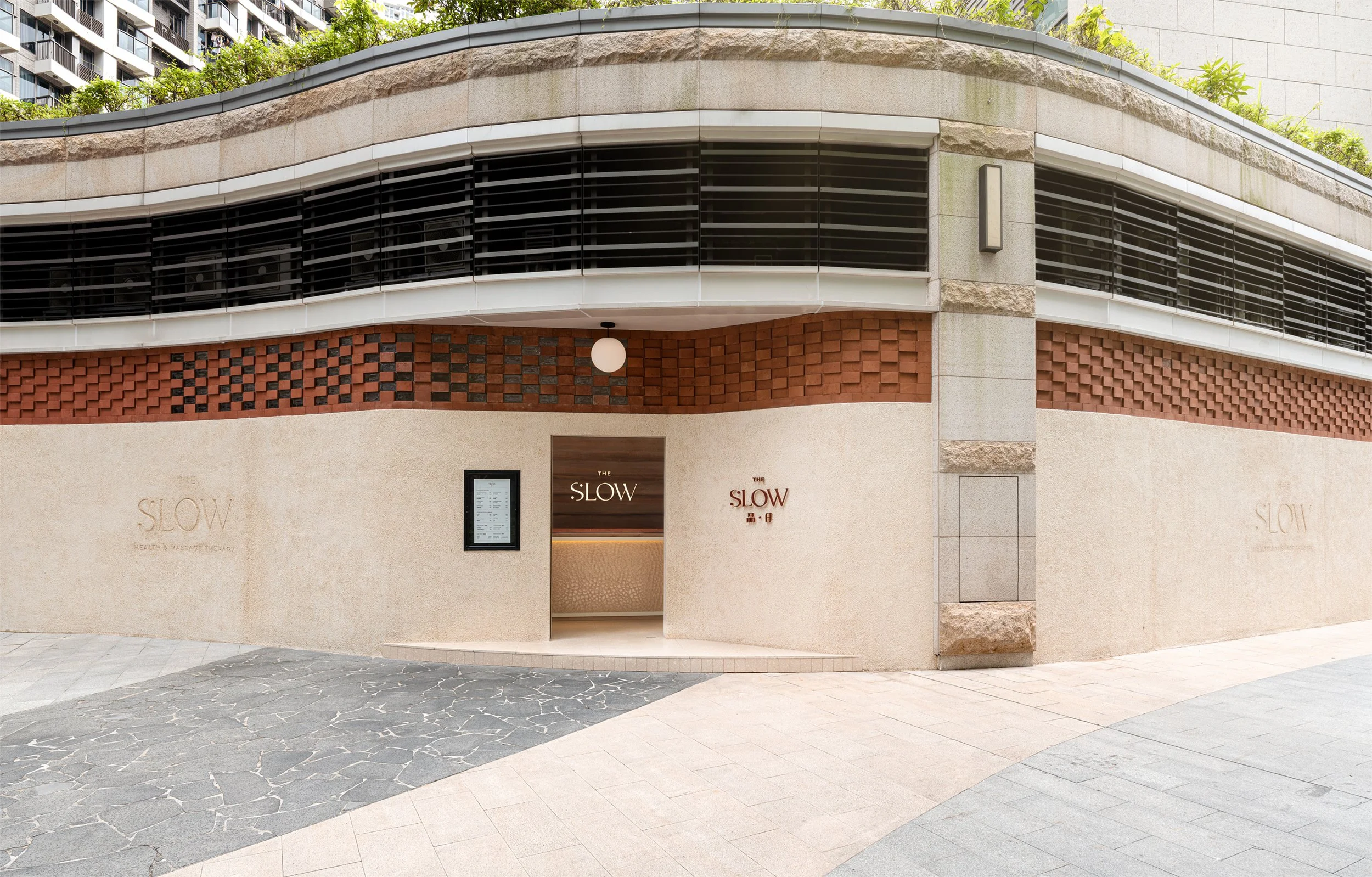 Street view of the entrance to a restaurant called The Slow with beige walls, red brick accents, a black framed menu display, and a wooden sign reading The Slow.