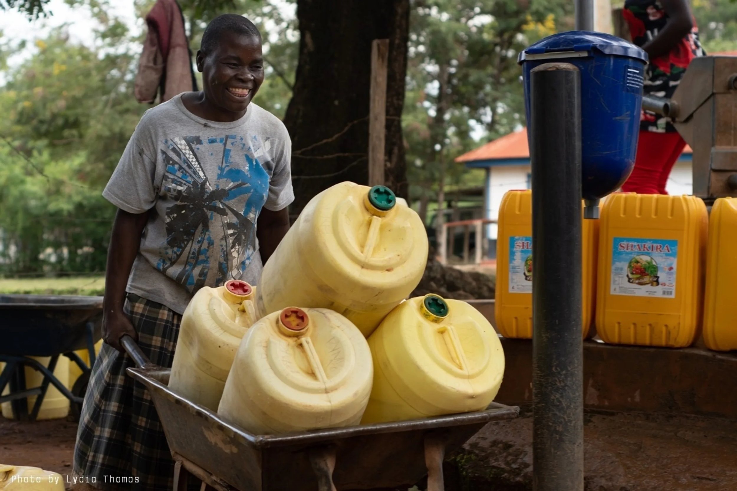 Woman wheels jerrycans to one of Evidence Action’s chlorine dispensers