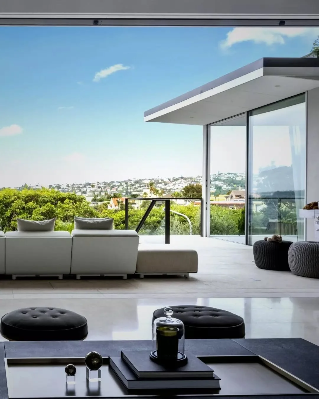 A generous living space opens entirely to the terrace through a 9-metre Swiss descending window, dissolving the boundary between interior and exterior. The room extends outward to a sheltered outdoor lounge beneath a deep roof overhang, where subtle 