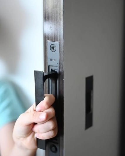 A pared-back sliding handle sits neatly within the door frame, its matte black finish set against the brushed metal channel. The handle seamlessly disappears when not in use, 

Integrated at hand height, the detail reflects a quiet emphasis on restra