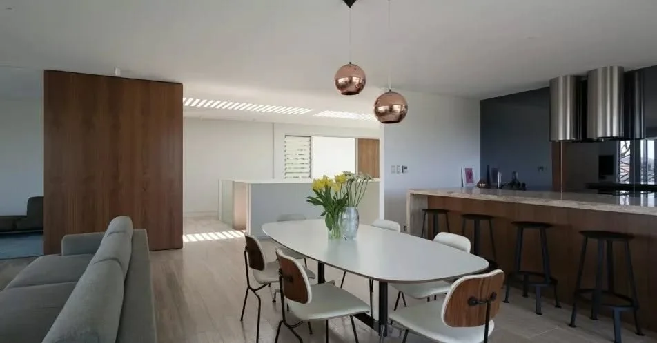 An open-plan living, dining and kitchen space is organised as a continuous interior, with each element arranged to maintain clarity and flow. The dining setting sits centrally within the plan, connecting the more enclosed living area to the kitchen b