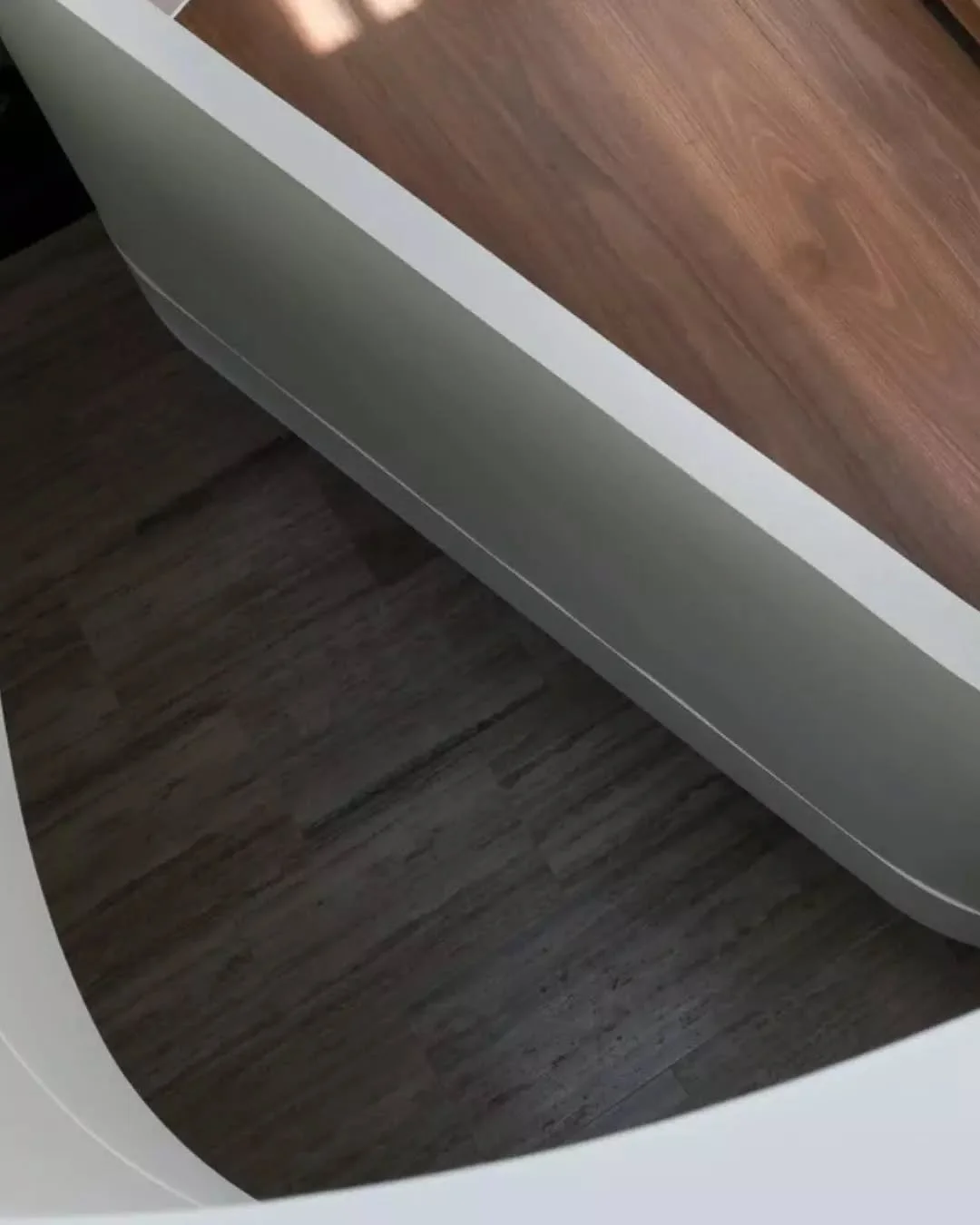 A close view of the stair reveals the junction between materials, where the curved white balustrade folds seamlessly into the timber tread. The balustrade is expressed as a single surface, with transitions carefully controlled to maintain a crisp, co