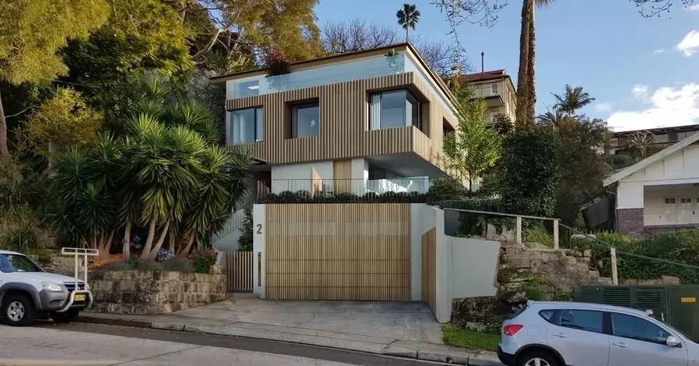 Set within a sloping site, this reworked property retains its original structure while introducing a refined material palette that redefines its street presence.

A timber-clad upper level sits above a grounded base, with vertical battens wrapping th