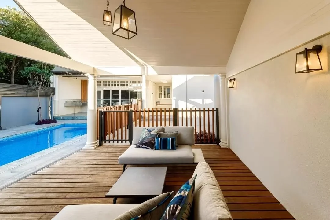 A pitched roof extends over the north-facing cabana, creating a sheltered outdoor area overlooking the pool and surrounding terrace. Timber decking runs throughout the space, with open edges maintaining clear sightlines across the outdoor living area