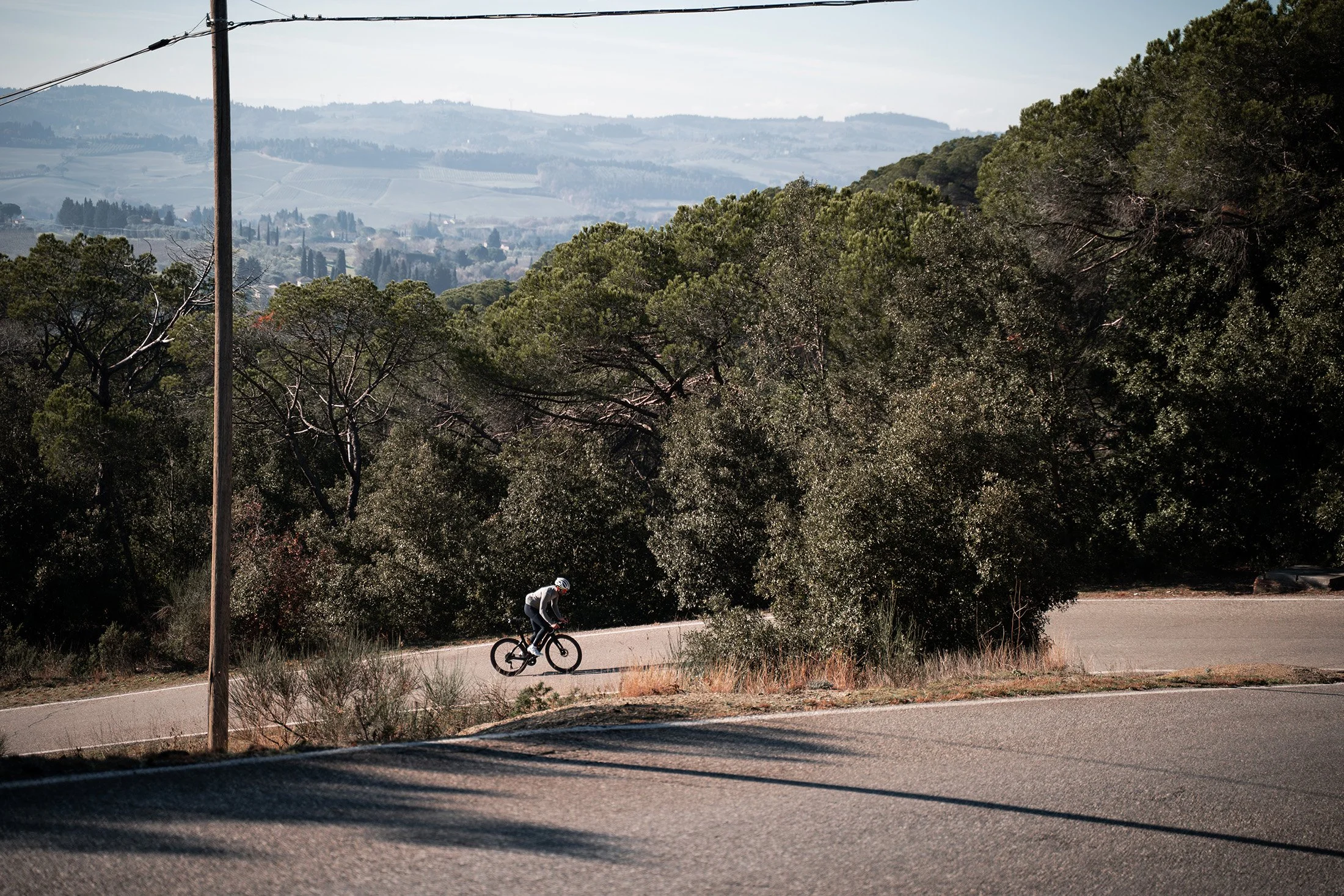 A person riding a mountain bike on a winding road through a wooded area with hills in the distance.