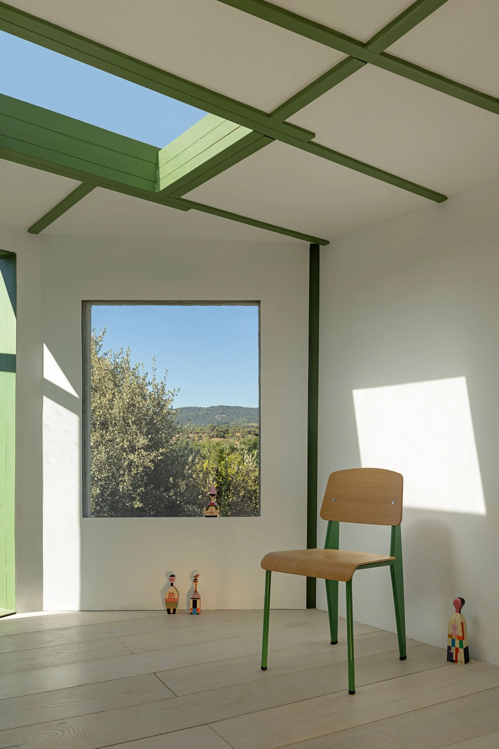 Standard Chair von Jean Prouvé, Holz mit grünem Untergestell, steht in Raum mit grünen Kanten. Wooden Dolls stehen auf dem Boden verteilt