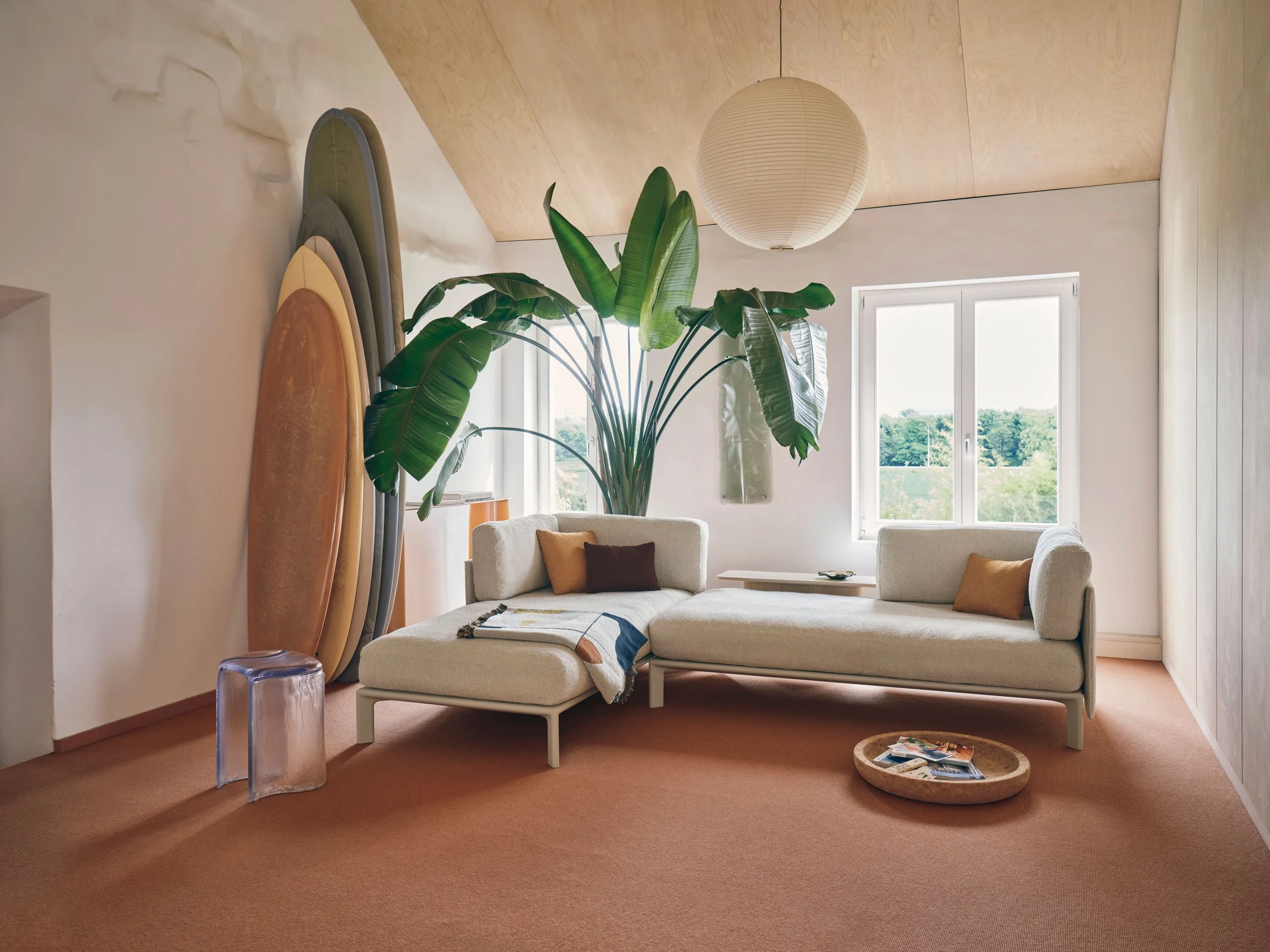 Der Künstler Lukas Cober und die Ärztin Vera Köller wohnen in Maastricht in einem ehemaligen Bergarbeiterhaus. Wohnzimmer mit creme Sofa. Surfbretter an Wand, grosse Pflanze in Ecke. Decke Akari Leuchte und Cork Bowl an Boden