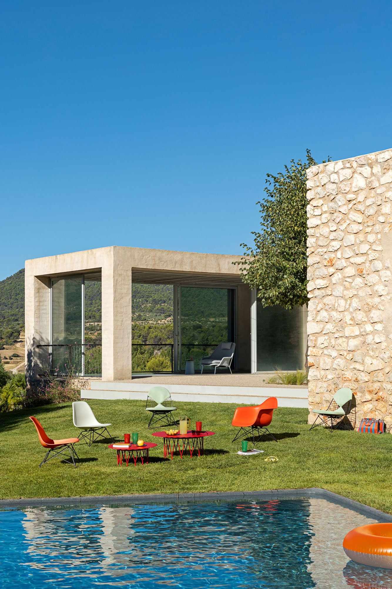 Outdoor Lounge in Wiese mit Eames Plastic- und Wire Chairs Lounge Sesseln. Pool ist im Vordergrund.