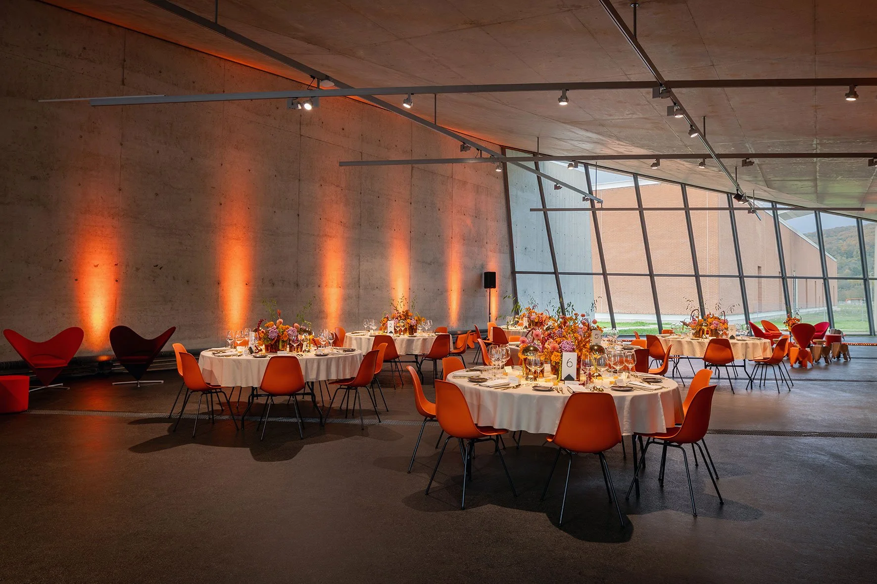 Das Gestaltungskonzept für das VIP-Dinner übersetzte die Farben und Formen des Doshi Retreats sowie die Atmosphäre des indischen Lichterfestes Diwali in eine europäische, zeitgemässe Ästhetik. orange Eames Plastic Stühle, farbige Blumen, oranges Lich