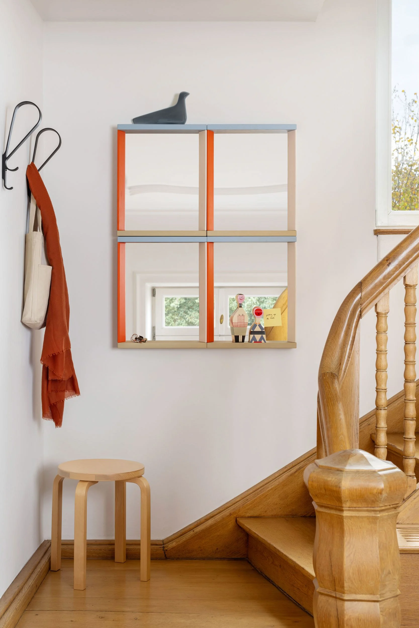 Color Frame Mirror. Vier Spiegel in orange/hellblau an Wand bei Treppenaufgang. Links an Wand ist eine Garderobe mit orangem Schal und Tasche. Artek Hocker Holz in Ecke