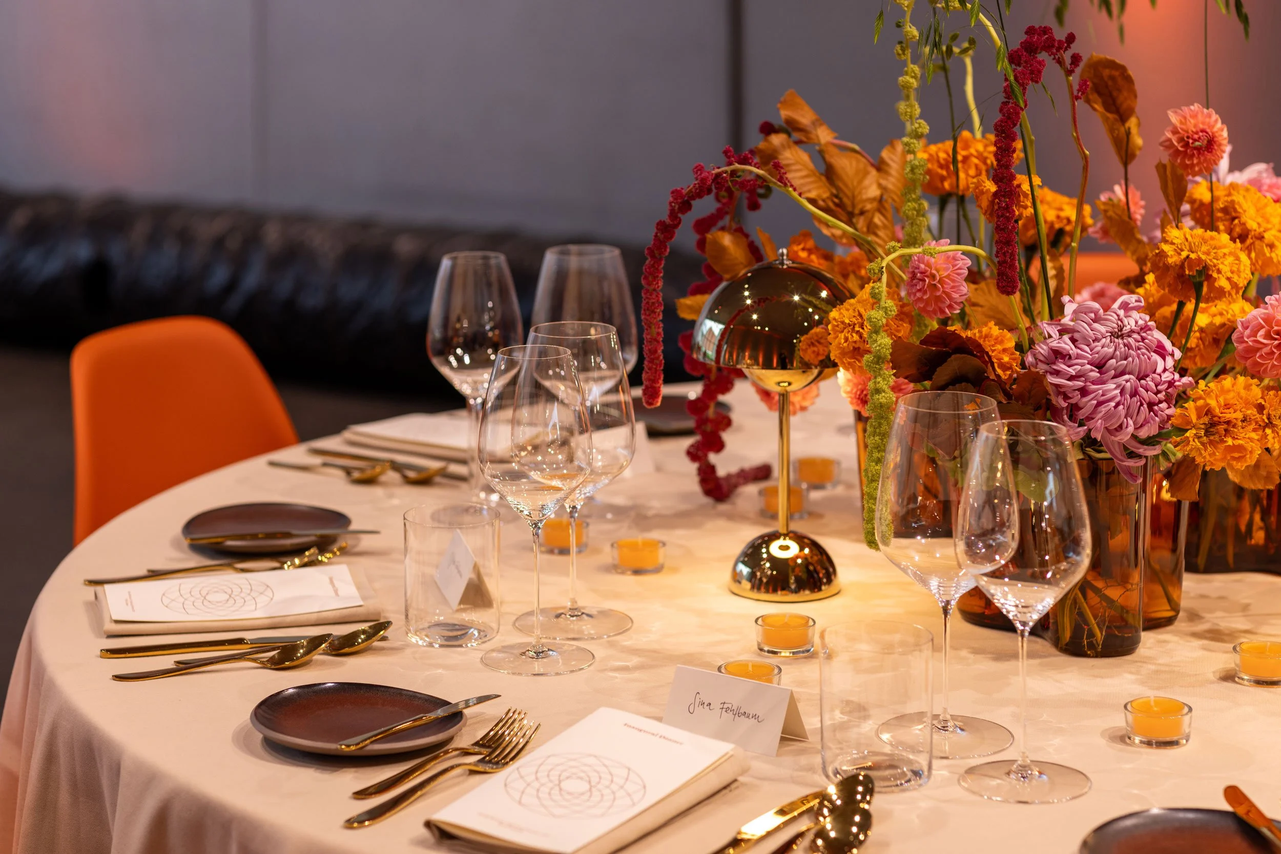 Das Gestaltungskonzept für das VIP-Dinner übersetzte die Farben und Formen des Doshi Retreats sowie die Atmosphäre des indischen Lichterfestes Diwali in eine europäische, zeitgemässe Ästhetik. orange Eames Plastic Stühle, farbige Blumen, oranges Lich