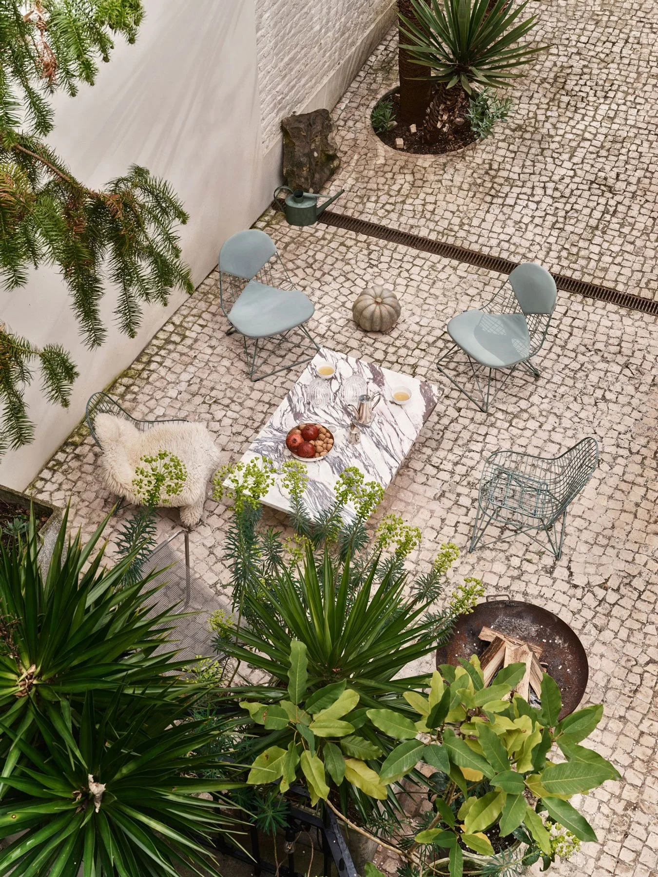 Home Stories for Winter 25 wurden beim Architekten David Van Severen und der Modefotografin Martina Bjorn fotografiert. Wire Chairs mit Bikini Outdoor im Garten. Marmortisch und Pflanzen daneben.