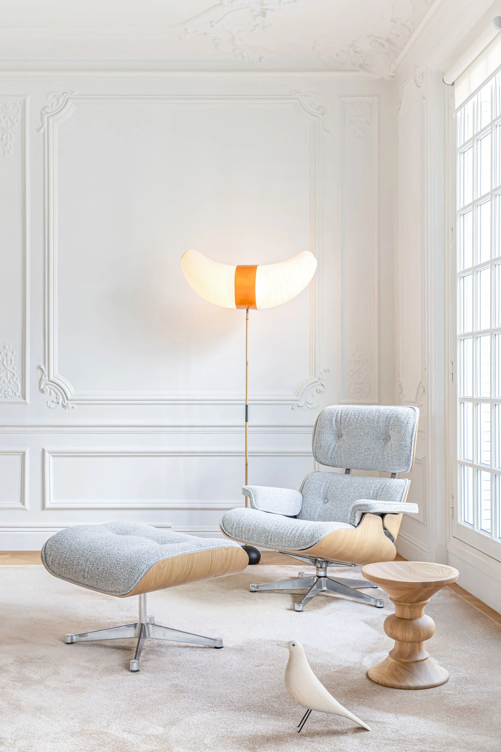 Lounge Chair in Stoff vor weisser Wand mit Stuckaturen, Eames Hocker und Eames House Bird in weiss auf Boden. Teppich in creme