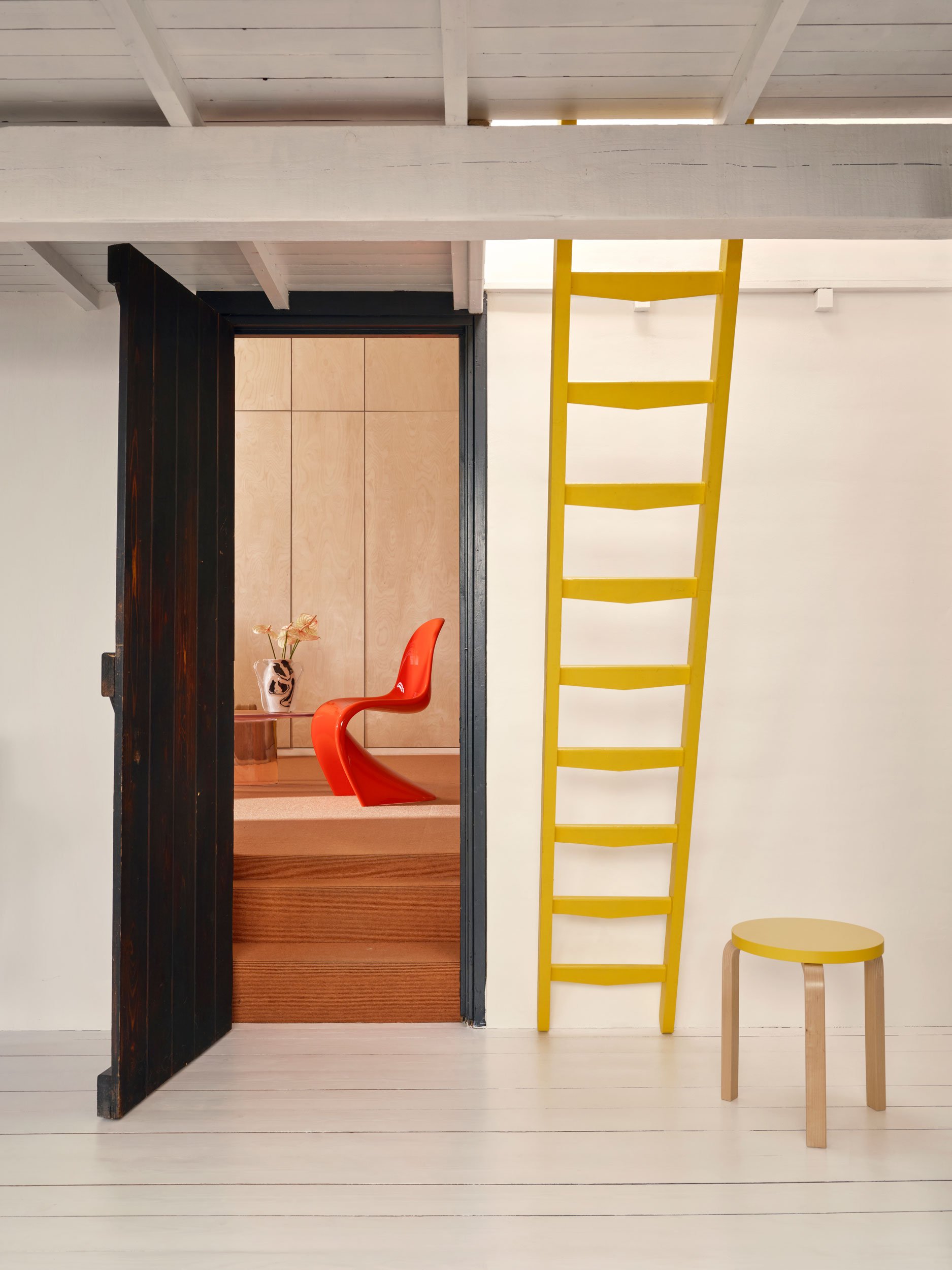 Der Künstler Lukas Cober und die Ärztin Vera Köller wohnen in Maastricht in einem ehemaligen Bergarbeiterhaus. Sicht in Raum mit rotem Panton Chair. Vorne gelbe Treppe mit gelbem Artek Hocker