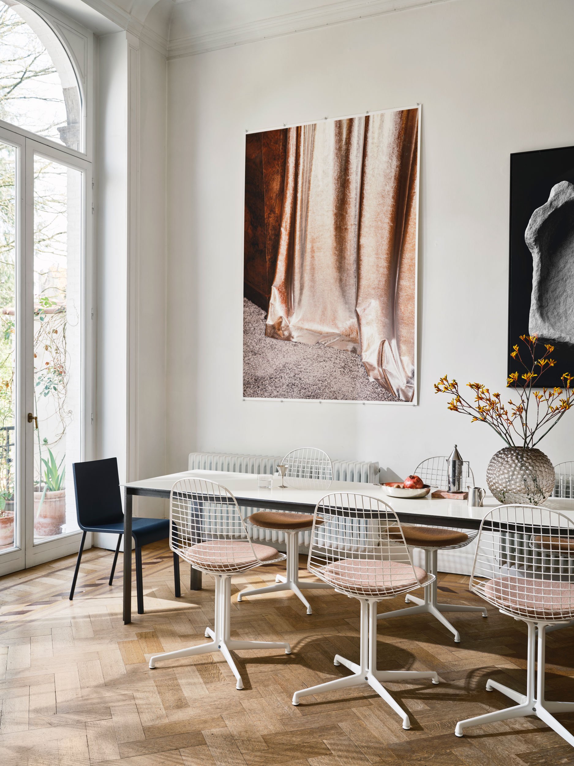Home Stories for Winter 25 wurden beim Architekten David Van Severen und der Modefotografin Martina Bjorn fotografiert. weisse Wire Chairs mit La Fonda Fuss an Esstisch mit zwei grossen Bildern an Wand