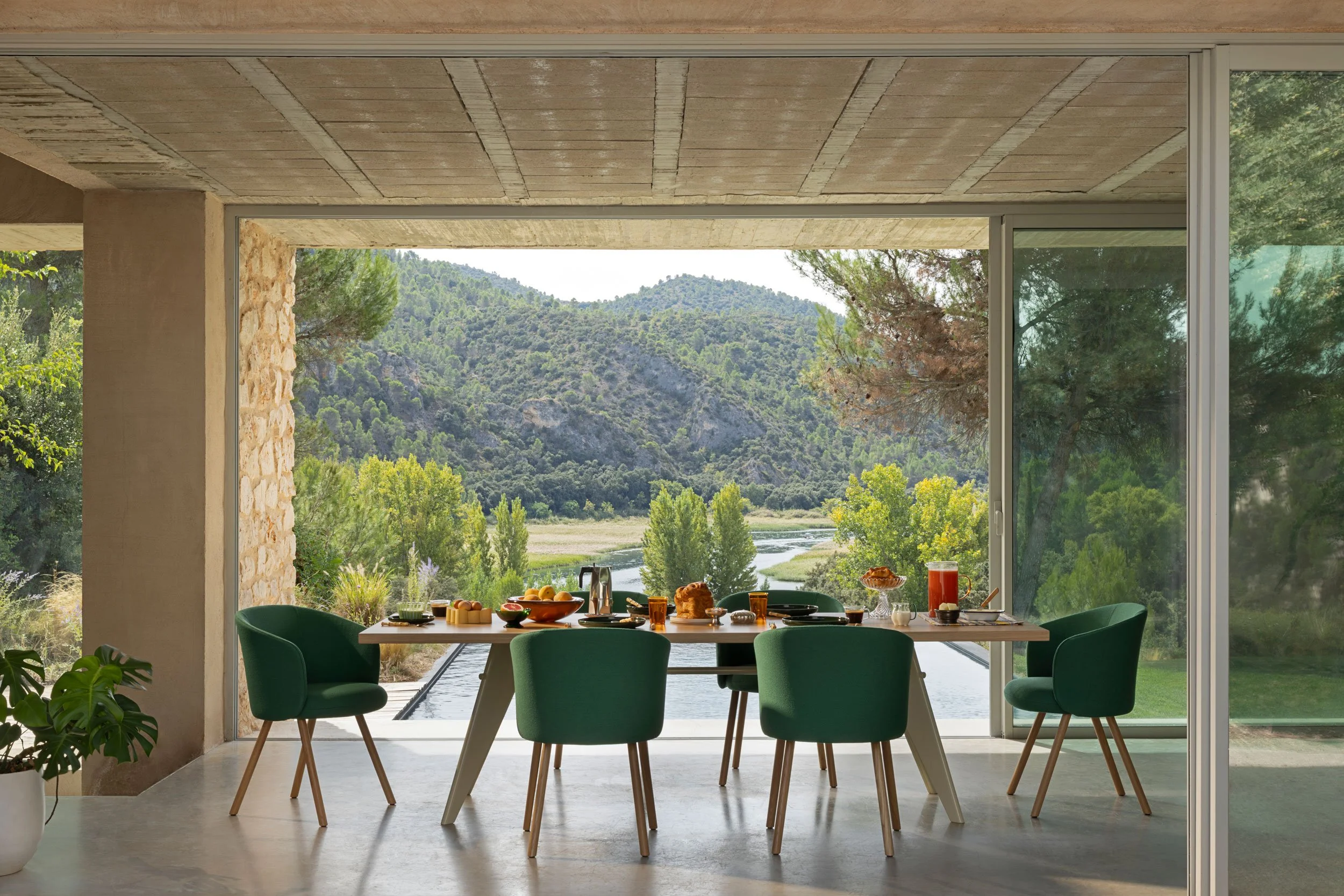 Esstisch mit Mikado Stühlen. Im Hintergrund grosses Fenster mit Aussicht ins Grüne. Der Tisch ist ein EM table von Prouvé