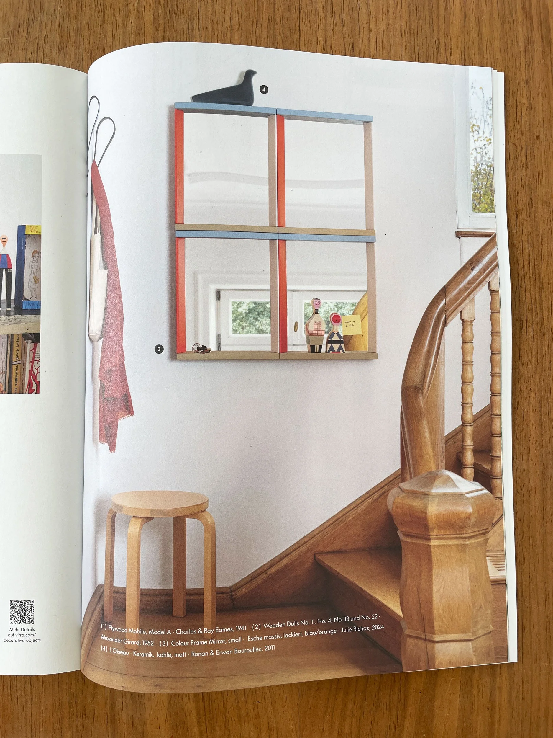 Color Frame Mirror im Katalog. Vier Spiegel in orange/hellblau an Wand bei Treppenaufgang. Links an Wand ist eine Garderobe mit orangem Schal und Tasche. Artek Hocker Holz in Ecke